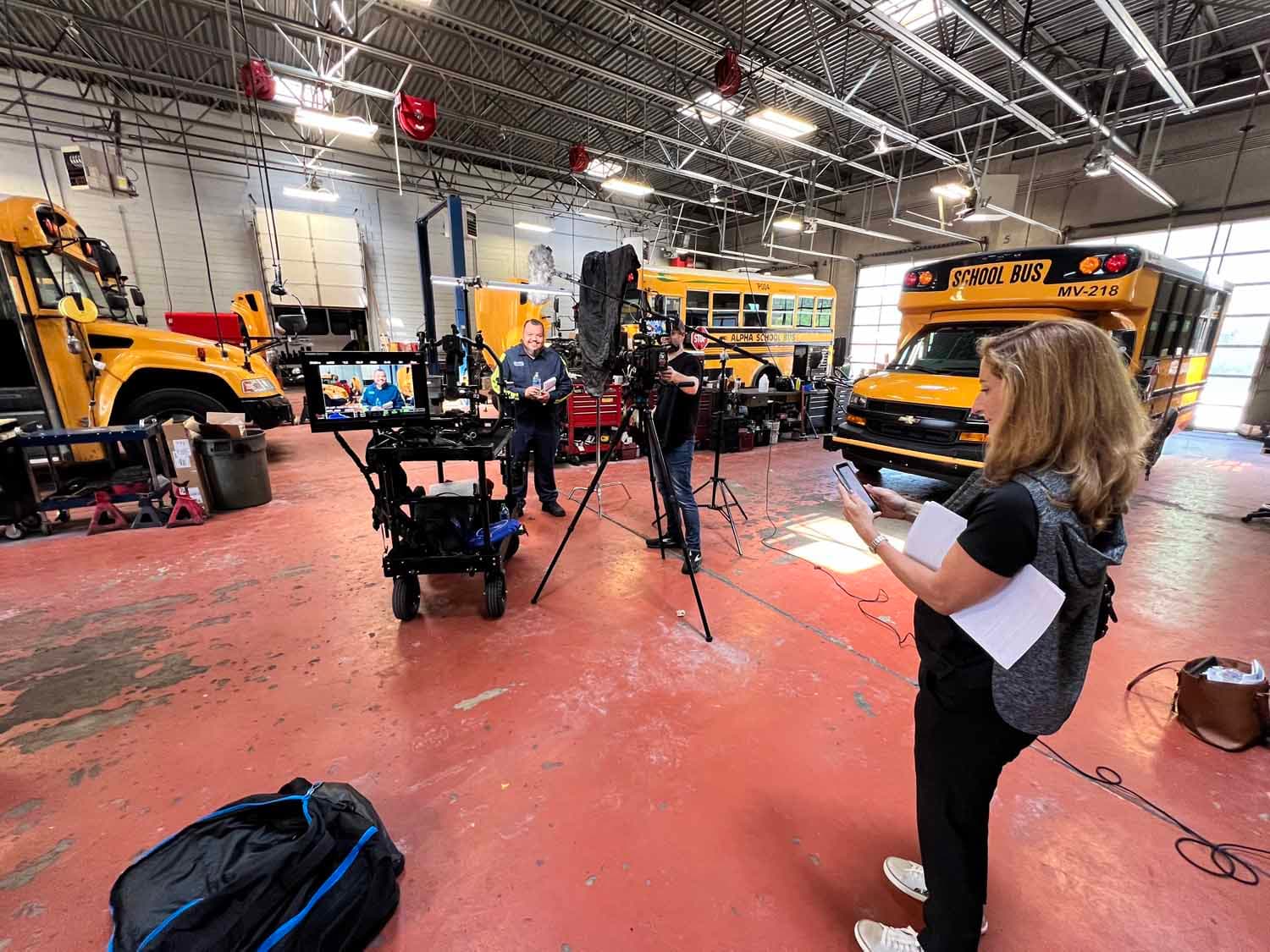 A behind-the-scenes look at a video production setup for a corporate video shoot inside a school bus machine shop.